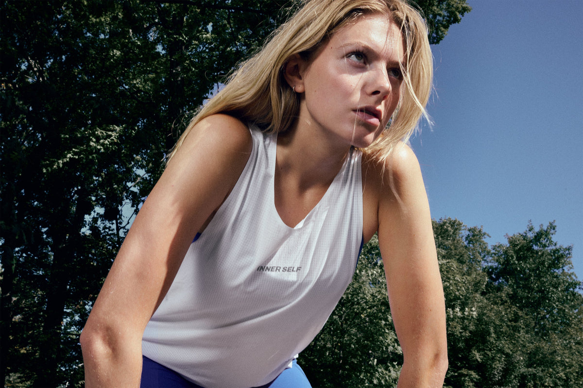 Model leaning forward outdoors in a white running singlet